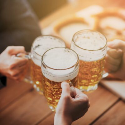 people, leisure and drinks concept - close up of hands clinking beer mugs at bar or pub S